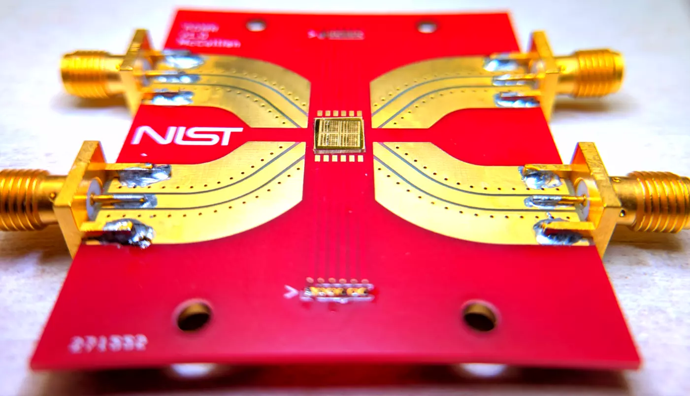 A bright-red rectangle with a NIST logo holds a gold-colored chip in the center with metal paths leading to connectors at the edge of the rectangle.